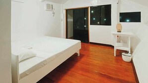 Een slaapkamer met een enkel bed, houten vloeren, een schuifdeur en een klein wit tafeltje met een vaas.