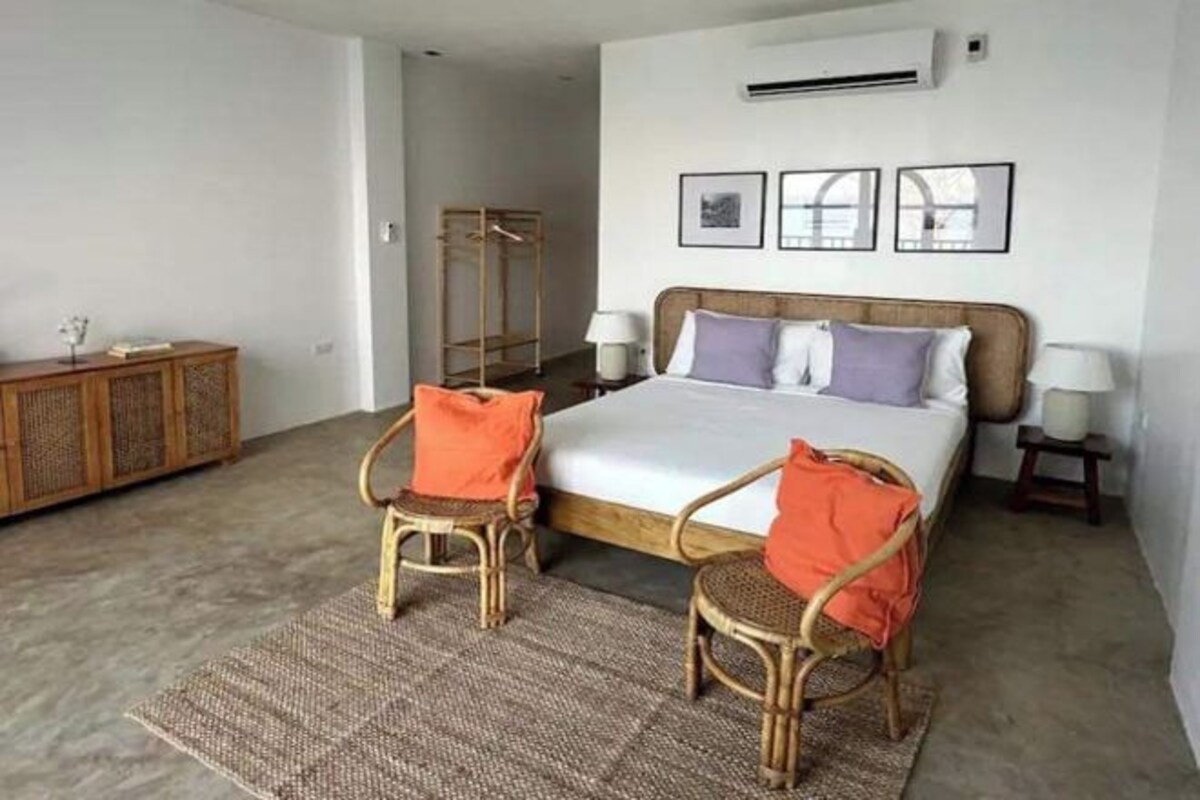 A bedroom with a bed, two chairs, a wardrobe, and a bedside table.