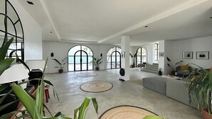 A spacious interior with large arched windows, a central seating area, and potted plants. - Uli Cliffhouse (Dasol)