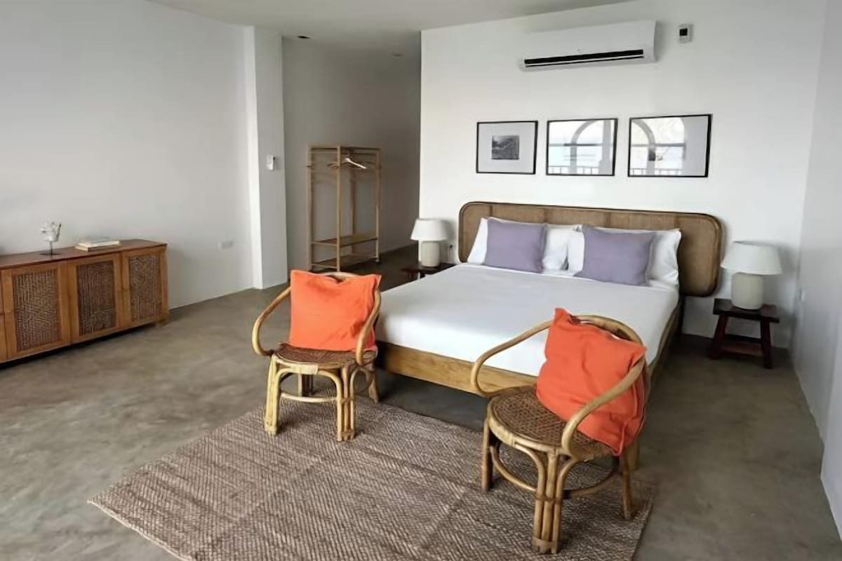 A bedroom with a bed, two chairs, a wardrobe, and a bedside table with lamps.