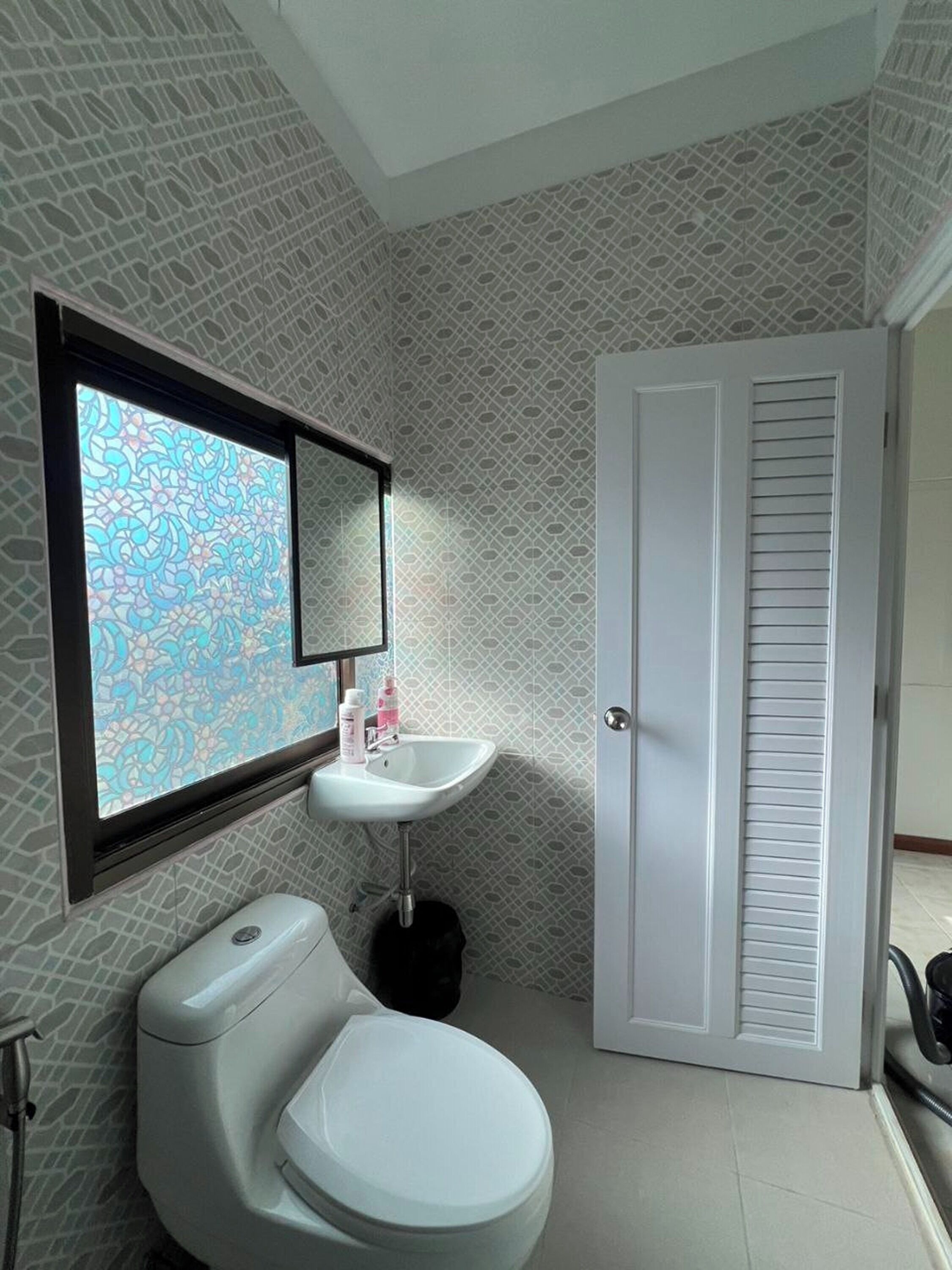 A bathroom with a toilet, sink, and a window with a patterned view.