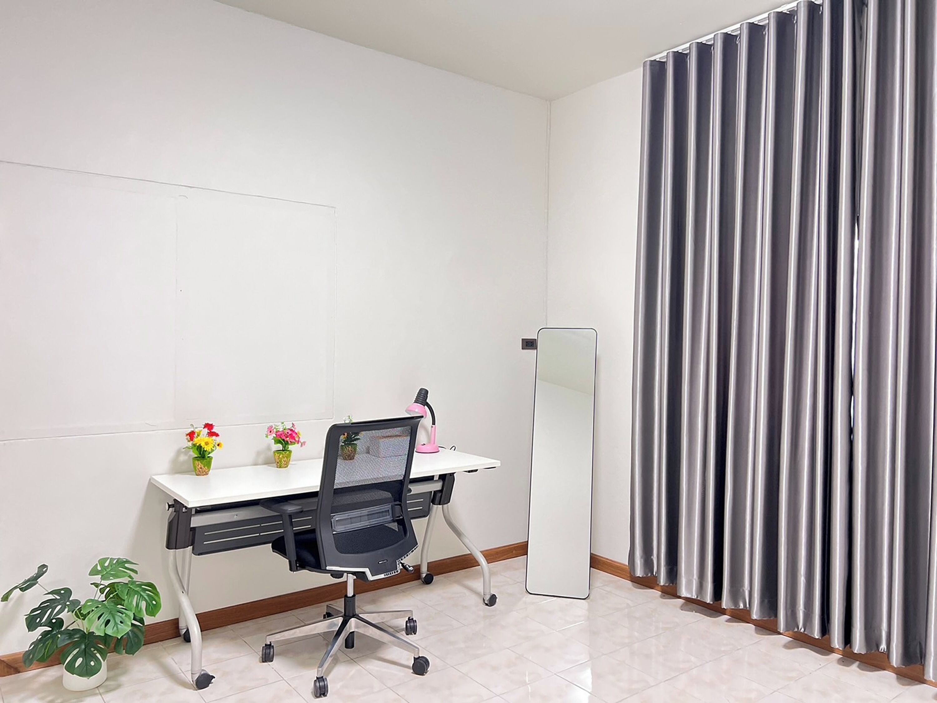 Een kleine kantoorruimte met een bureau, stoel, kamerplanten, een spiegel en een gordijn.