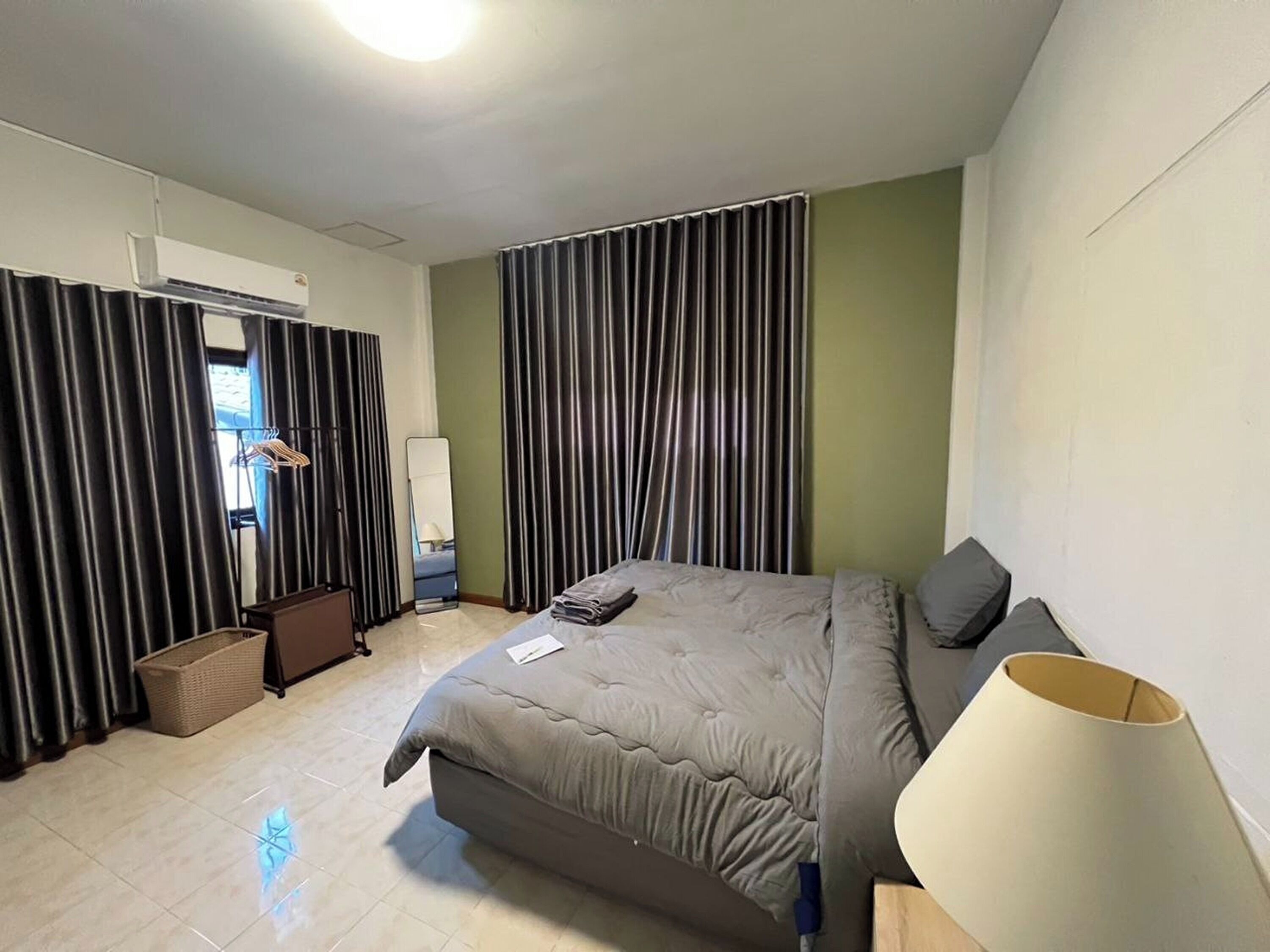 Ein Hotelzimmer mit Bett, Nachttischlampe, Spiegel, Kleiderschrank und einem Fenster mit Vorhängen.