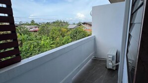 Un balcón con vistas a zonas verdes y casas, suelo de baldosas y pared blanca.