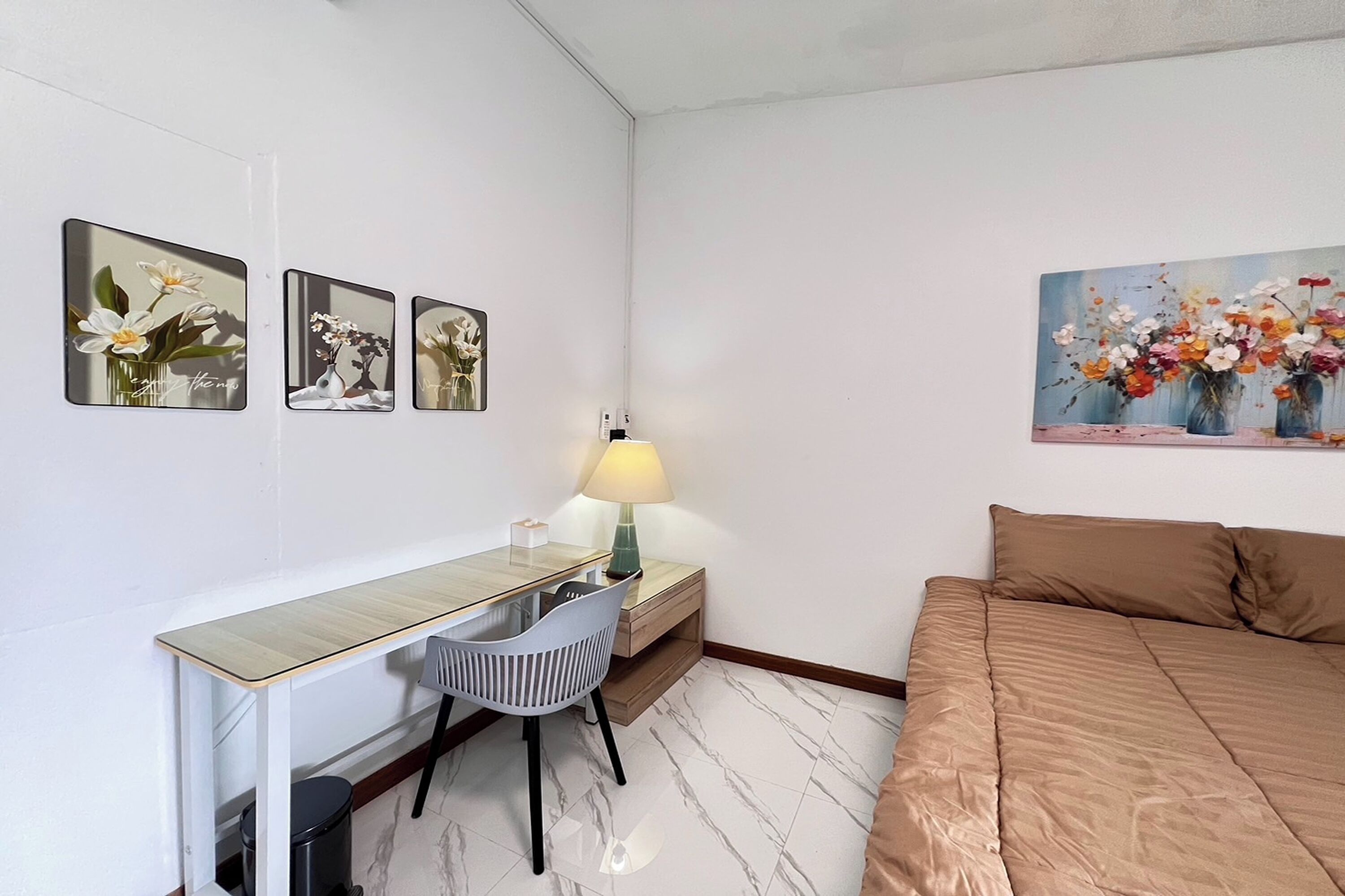 Un dormitorio con cama, escritorio con silla, lámpara y tres cuadros en la pared.