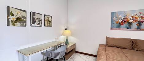 Un dormitorio con cama, escritorio con silla, lámpara y tres cuadros en la pared.