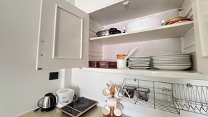 A kitchen with a white countertop, a coffee maker, a kettle, a rice cooker, a dish rack, and stacked plates. - Kuan Mapraw Villa 2 (Phatthalung)
