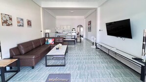 A modern living room with a brown leather sofa, a coffee table, and a flat-screen TV mounted on the wall. - Kuan Mapraw Villa 2 (Phatthalung)