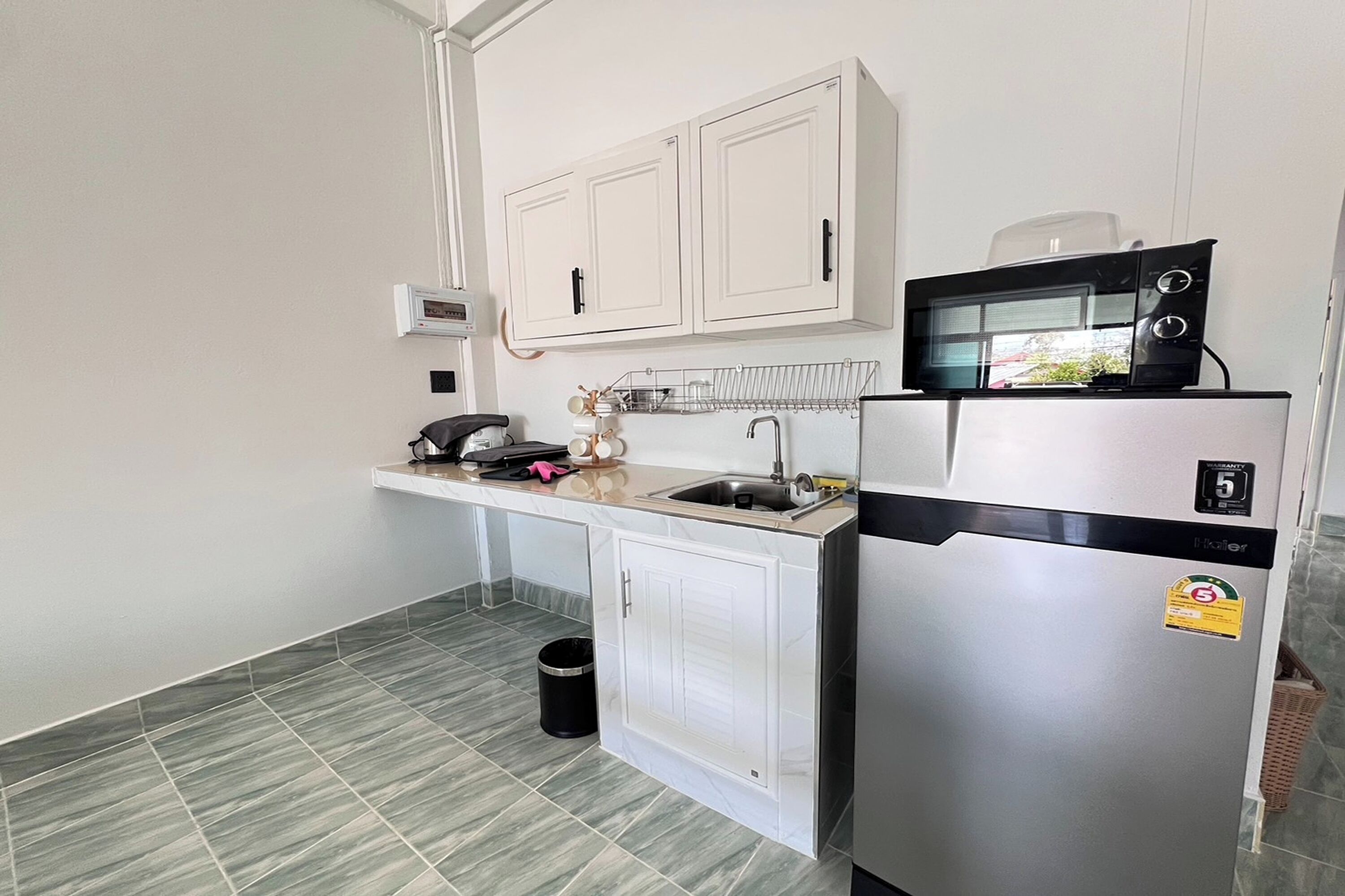 A compact kitchen with white cabinets, a stainless steel refrigerator, a microwave, and a sink.