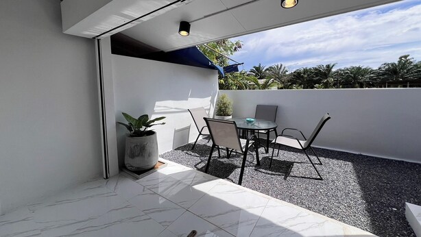 A modern outdoor patio with a table and chairs, a potted plant, and a view of the sky and trees. - Kuan Mapraw Villa 2 (Phatthalung)