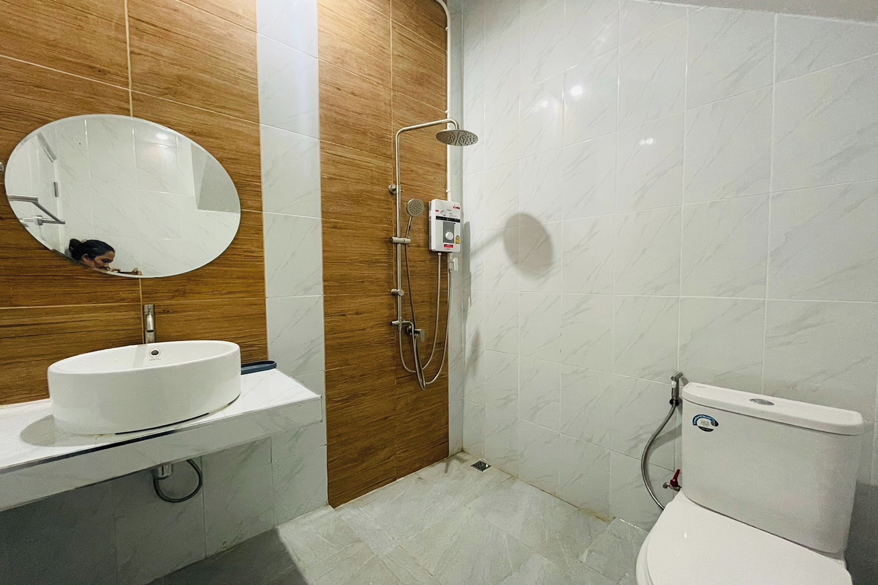 A bathroom with a wooden vanity, a round mirror, a toilet, and a shower.