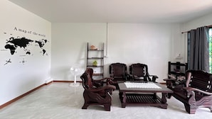 A modern living room with a world map wall art, a dining table with chairs, a standing fan, and a bookshelf. - Kuan Mapraw Villa 3 (Phatthalung)