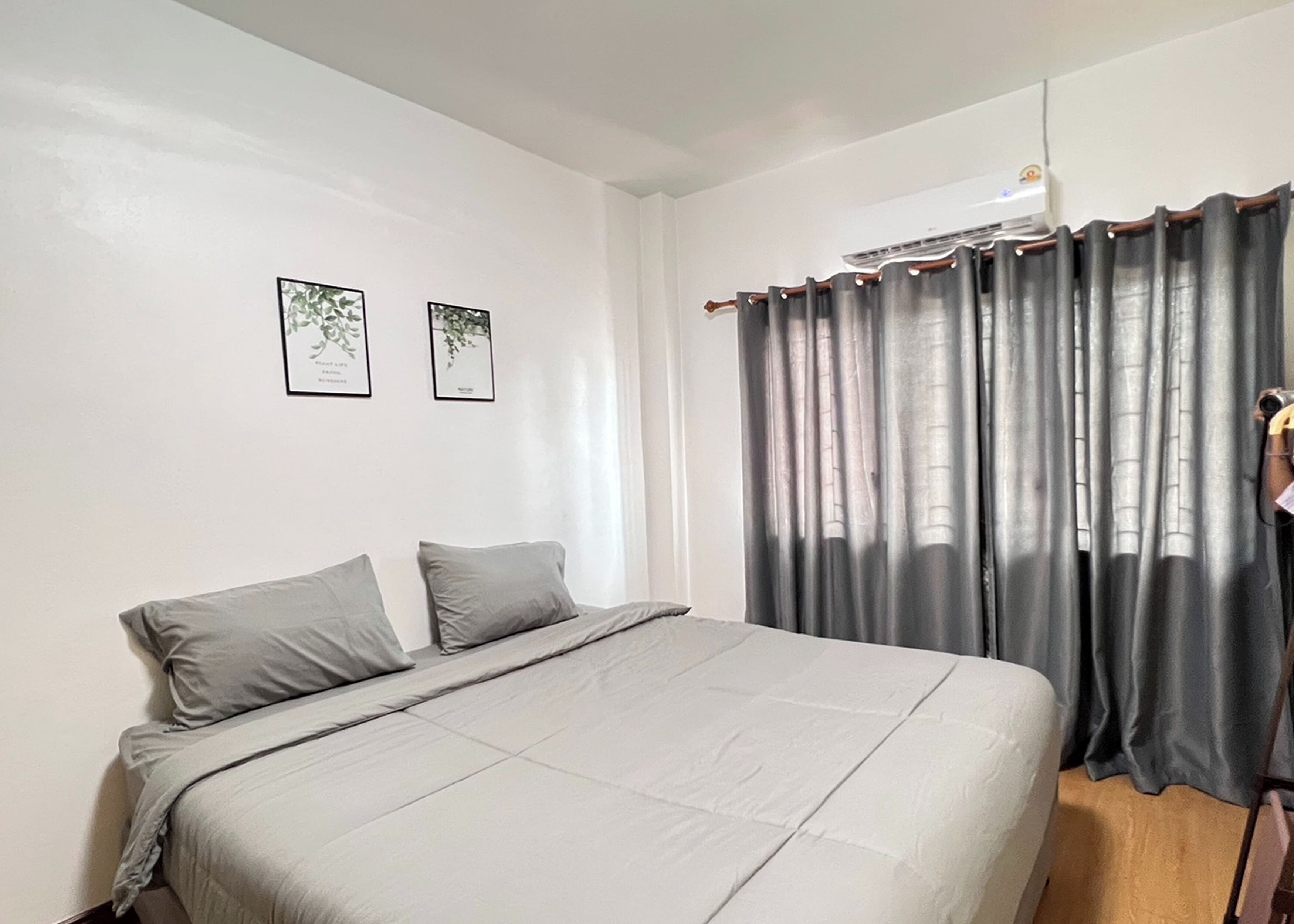 A bedroom with a bed, two pillows, a window with curtains, and two framed pictures on the wall.