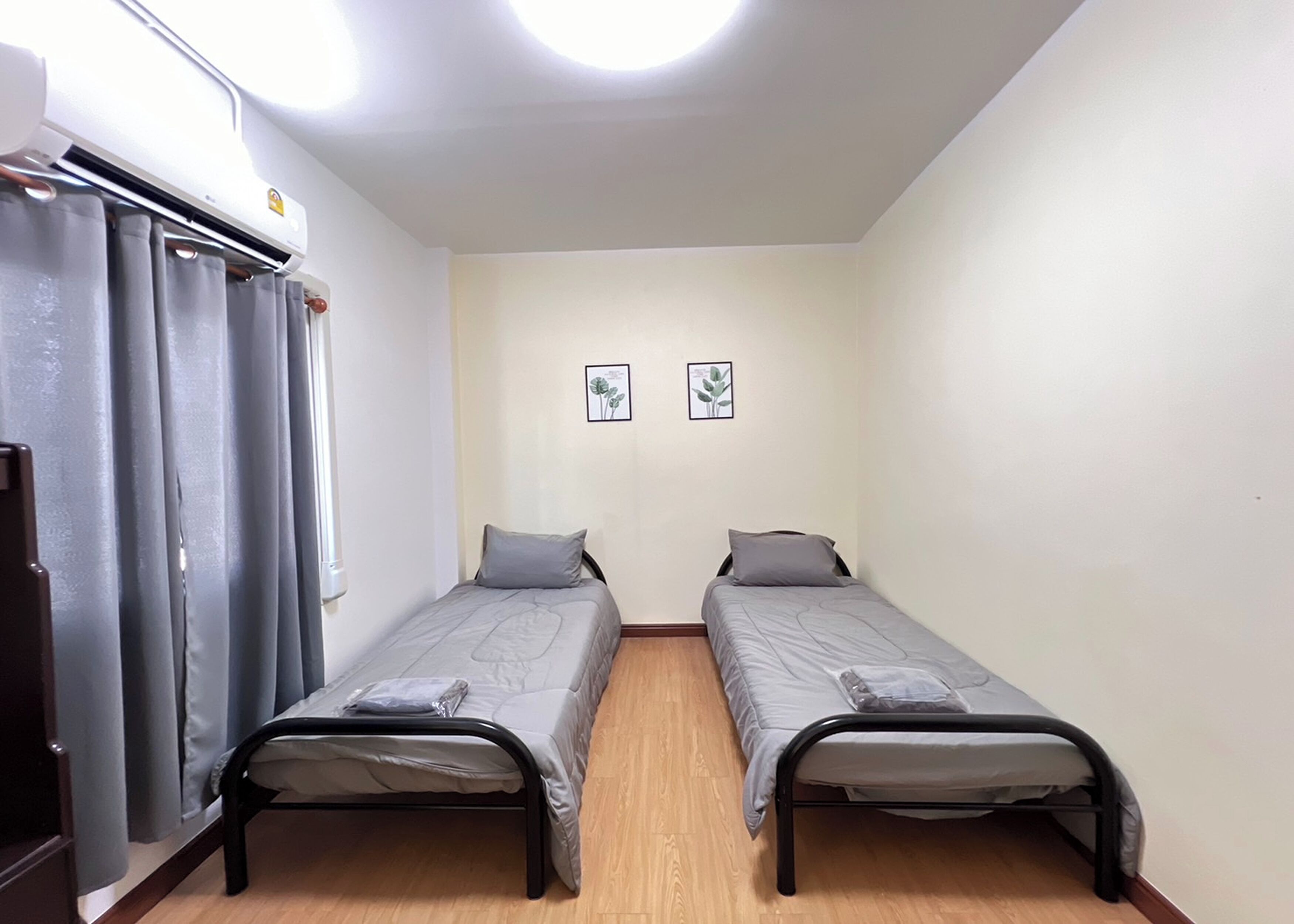 Een kleine, eenvoudige kamer met twee éénpersoonsbedden, een kledingkast en een plafondlamp.