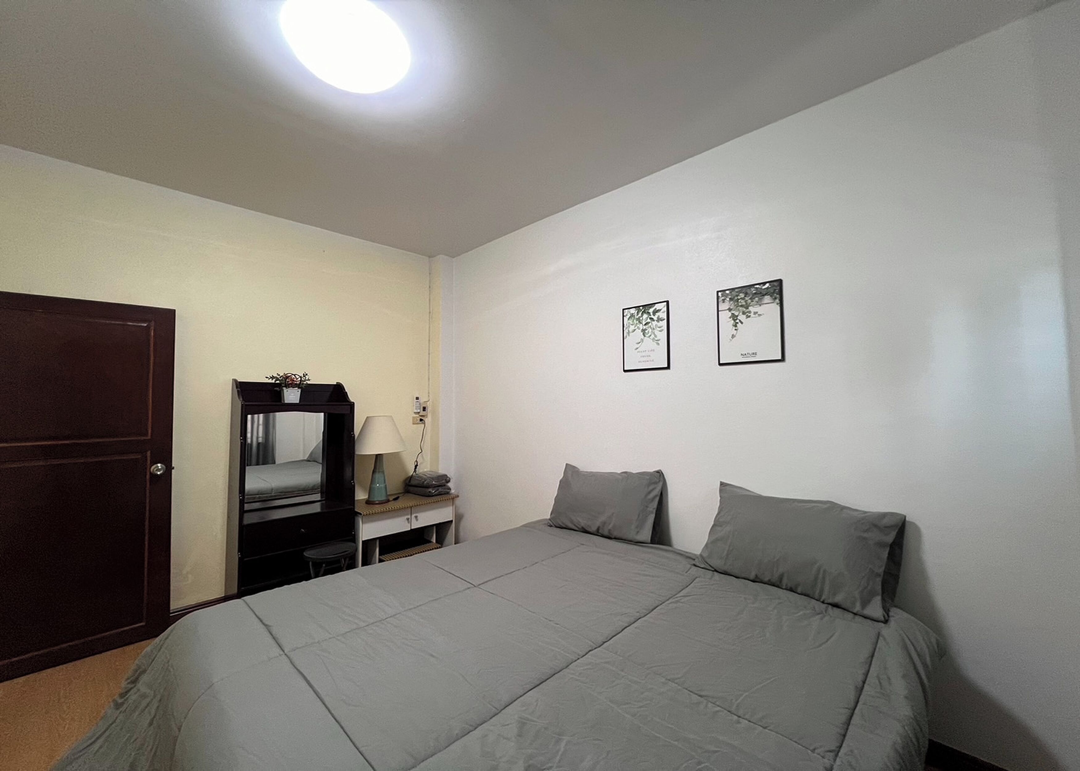 A bedroom with a bed, a desk, a chair, a lamp, and two framed pictures on the wall.