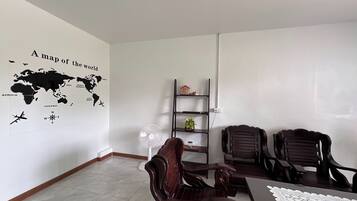 Un espacio de oficina moderno con un mapa mundial en la pared, un escritorio con una computadora portátil, dos sillas de madera, un estante pequeño con adornos y un ventilador de pie.