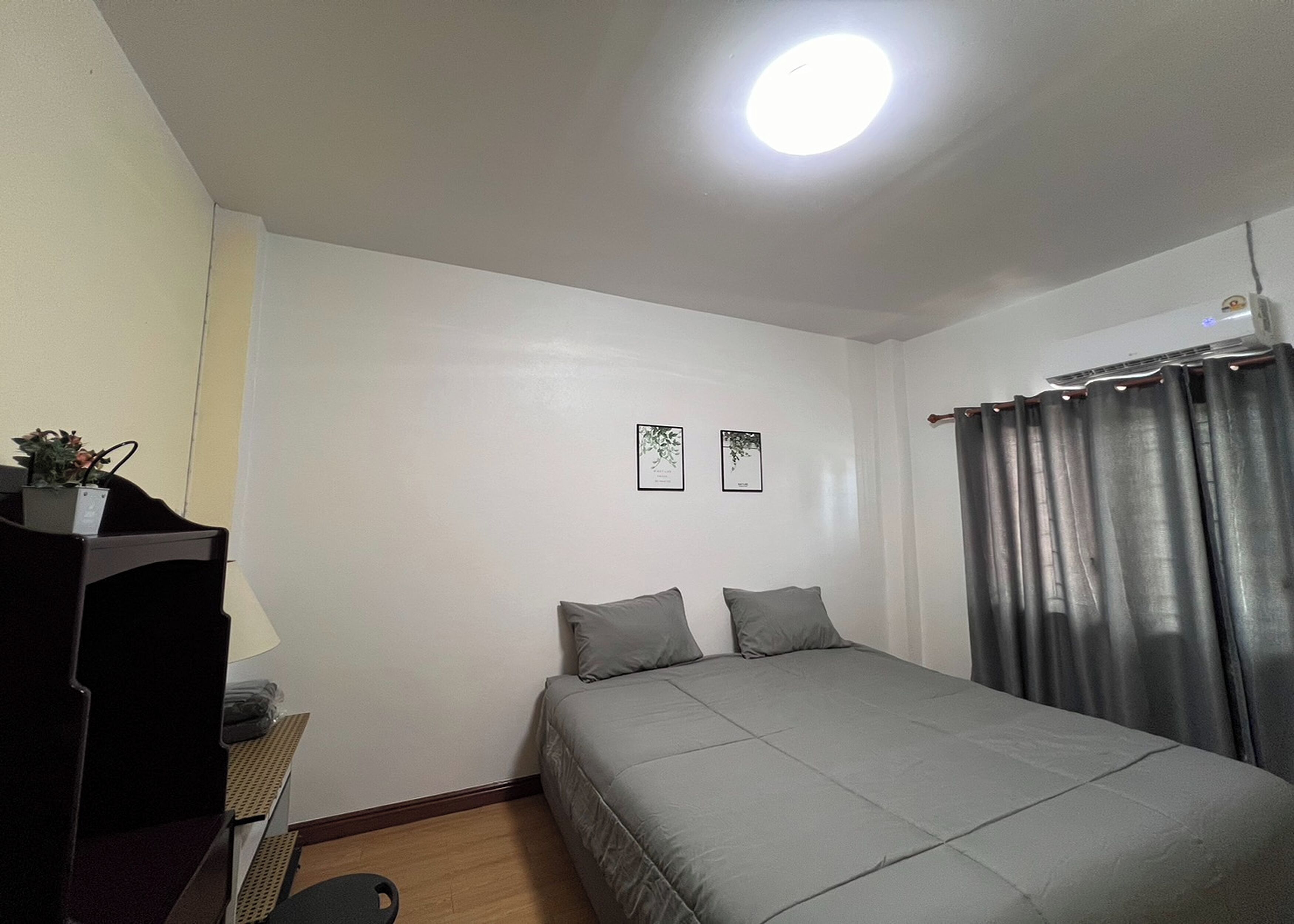 Un dormitorio pequeño y ordenado con una cama individual, un escritorio con silla, una planta en maceta y dos cuadros en la pared.