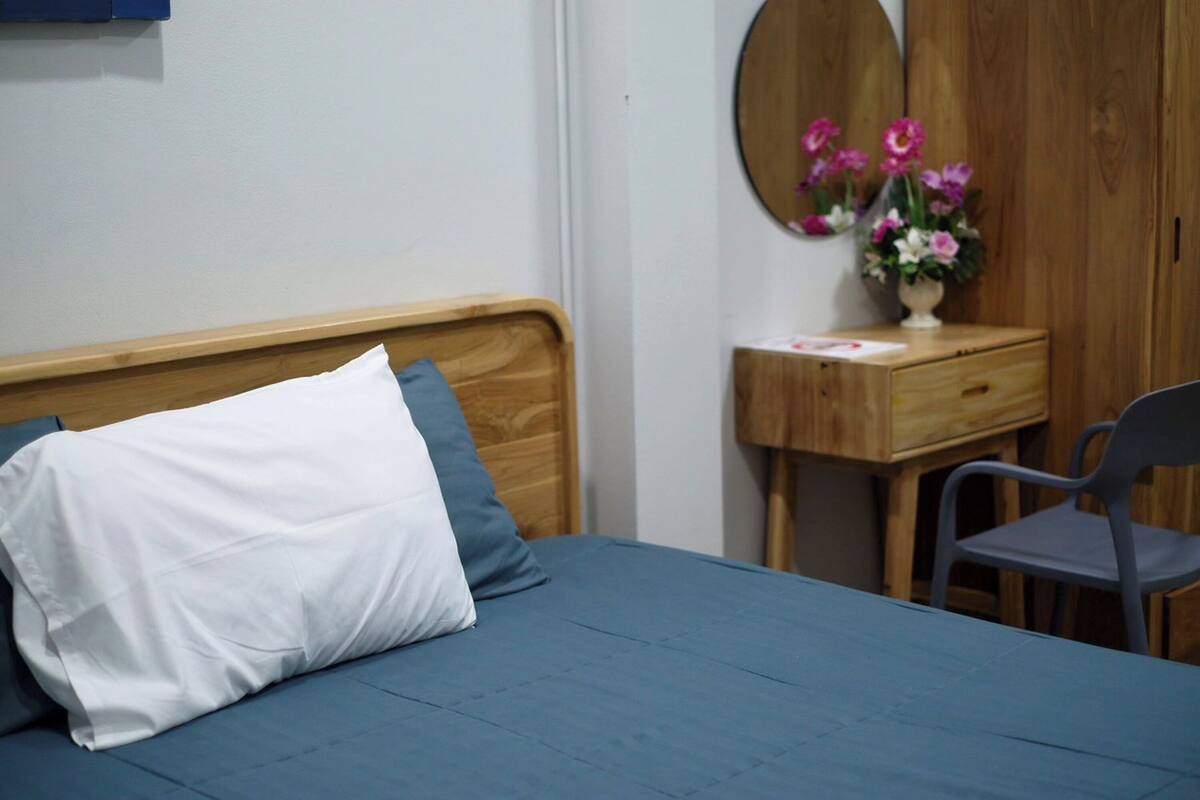 Um quarto com uma cama, cômoda de madeira, cadeira e espelho com flores.
