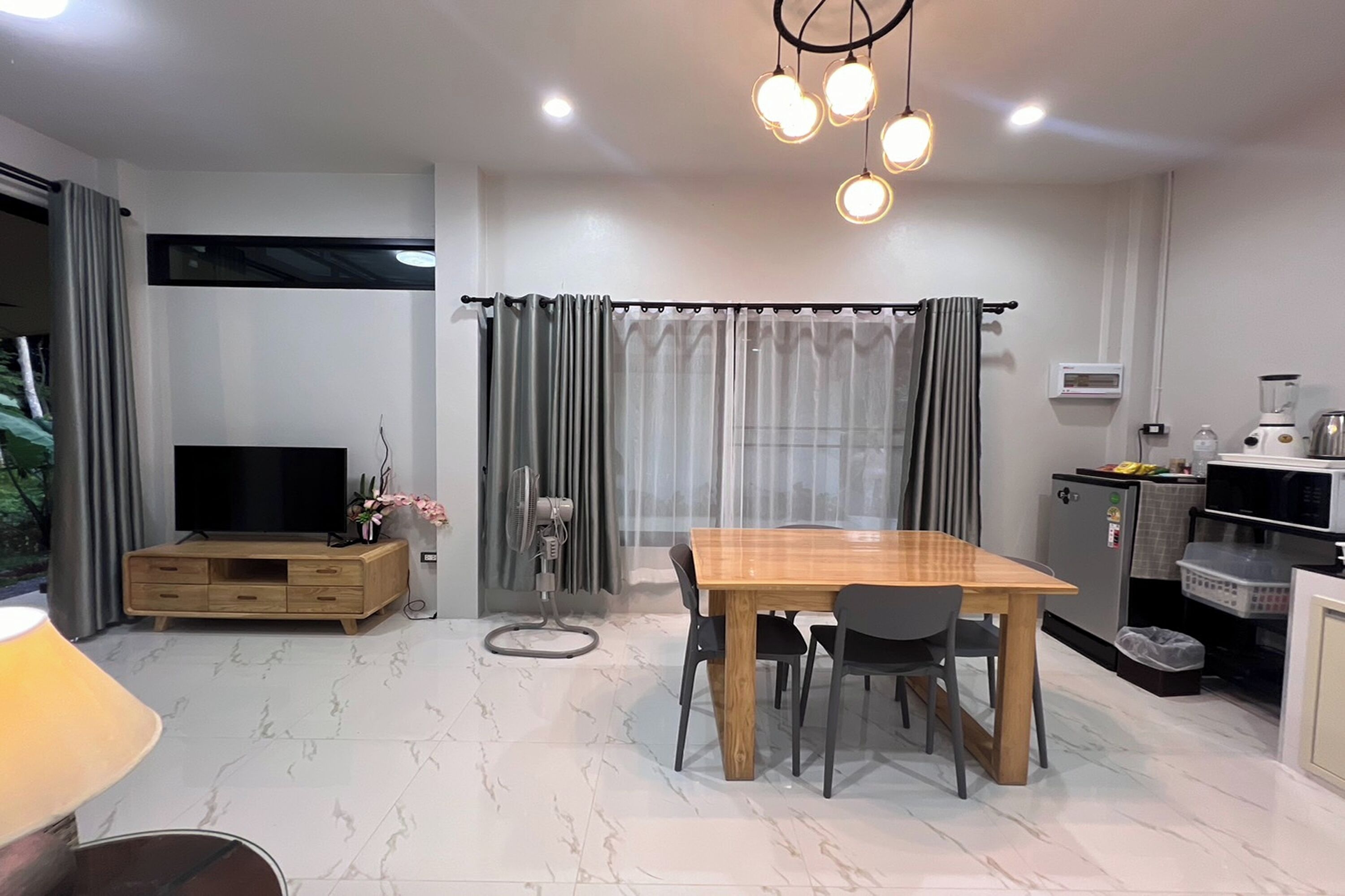 A modern living space with a dining table, chairs, a TV, and a kitchen area.