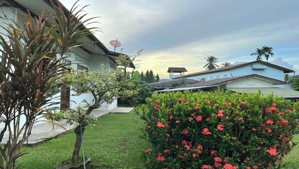 A residential area with a white house, a satellite dish, and a well-maintained garden with red flowers. - Baan Bonsuan Hill Guesthouse (Kathu)