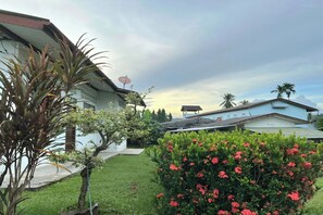 Una zona residencial con una casa blanca, una antena parabólica y un jardín bien cuidado con flores rojas.