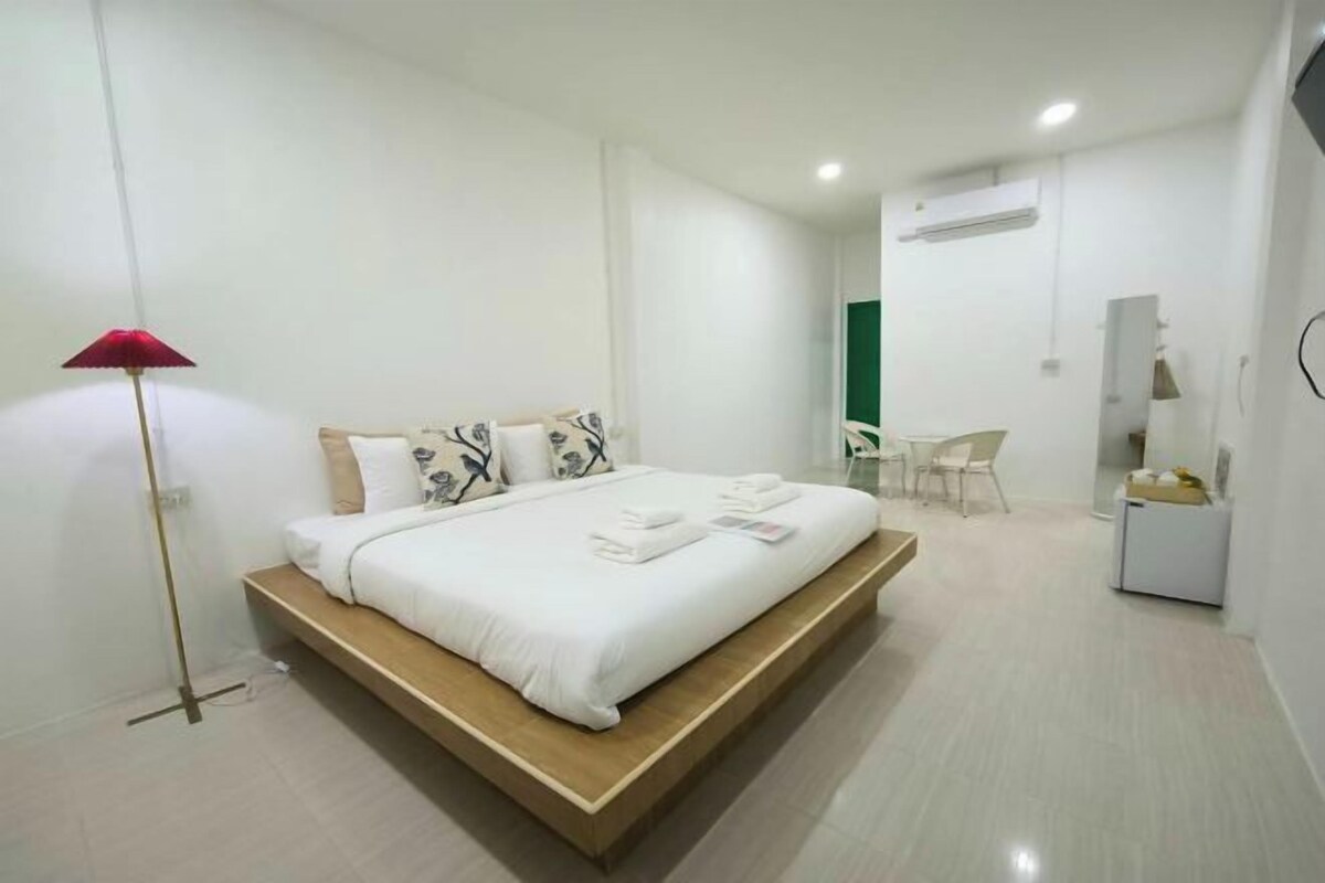 A modern bedroom with a wooden platform bed, white bedding, a red floor lamp, a small desk, and a chair.