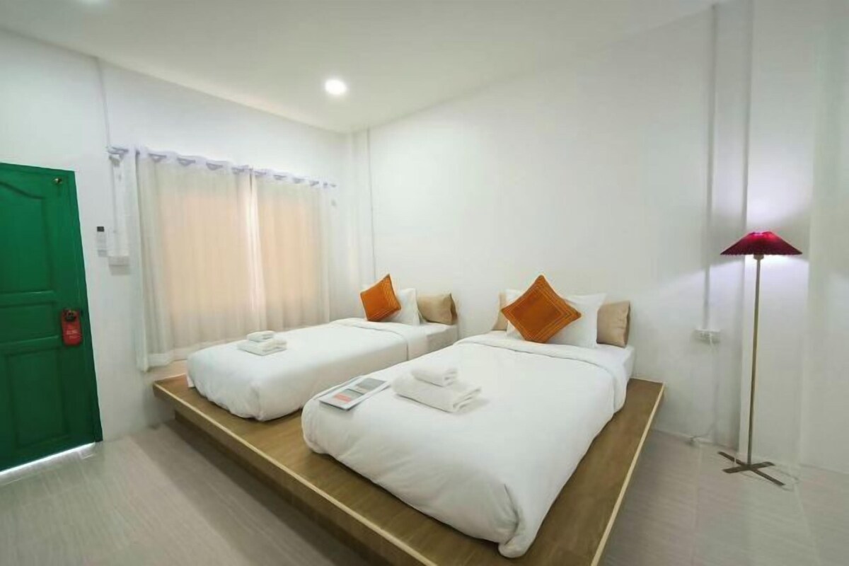 A hotel room with two beds, a green door, a floor lamp, and a window with curtains.