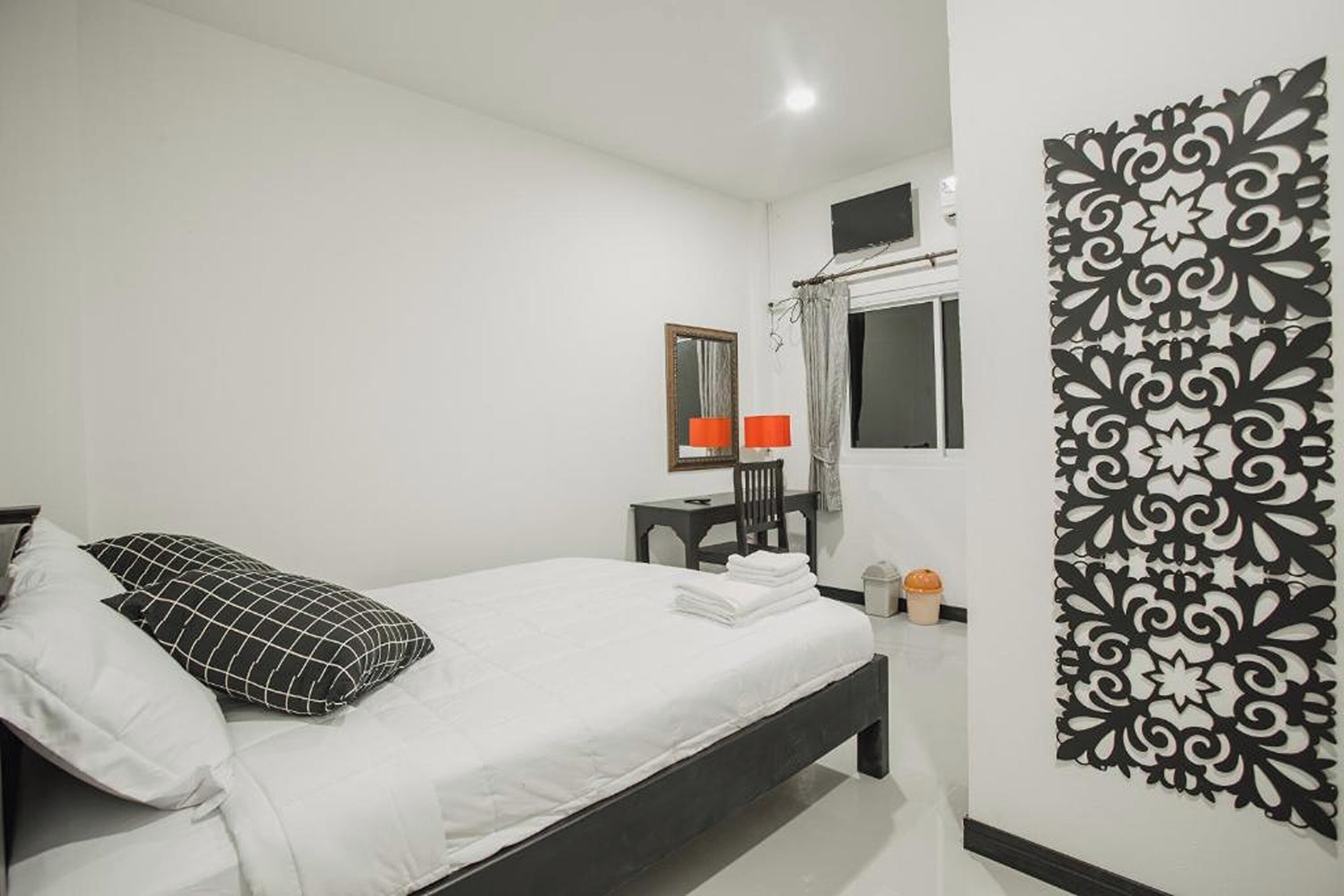 A neatly arranged bedroom with a bed, a chair, a small table, a mirror, and a decorative wall panel.