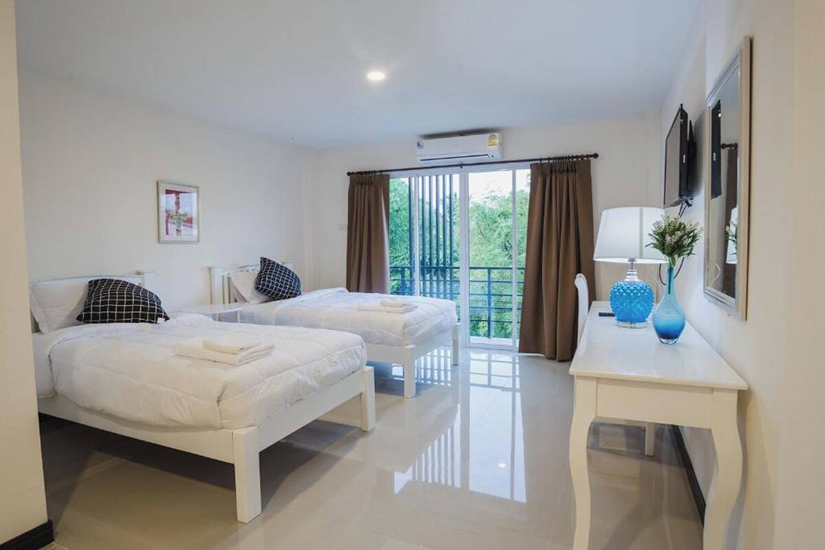 Una habitación de hotel con dos camas, una mesita con lámpara y un balcón con cortinas.