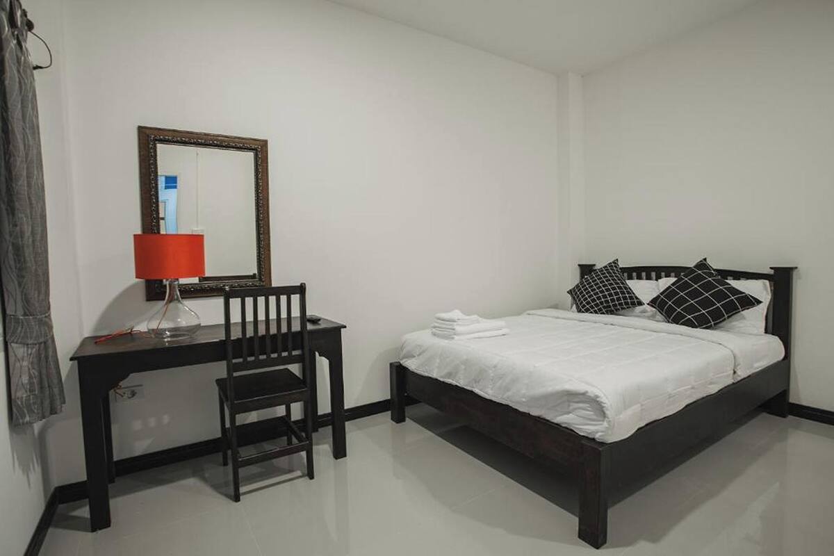 Un dormitorio con una cama, un escritorio con silla, una lámpara y un espejo.