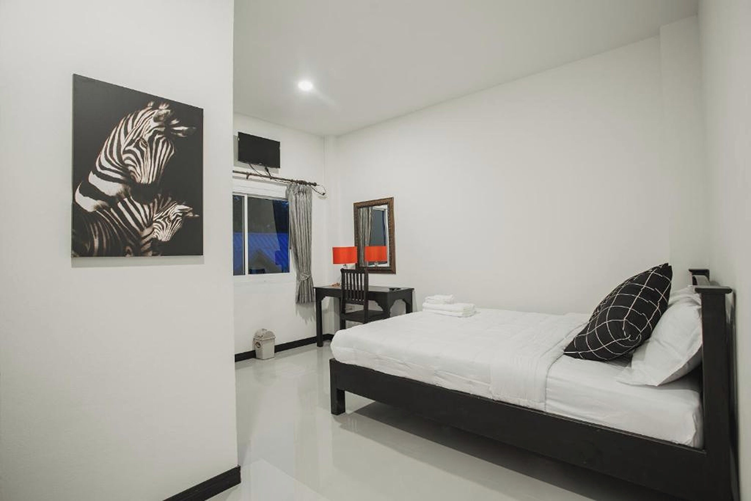 A bedroom with a bed, a desk, a chair, a window with curtains, and a zebra artwork on the wall.