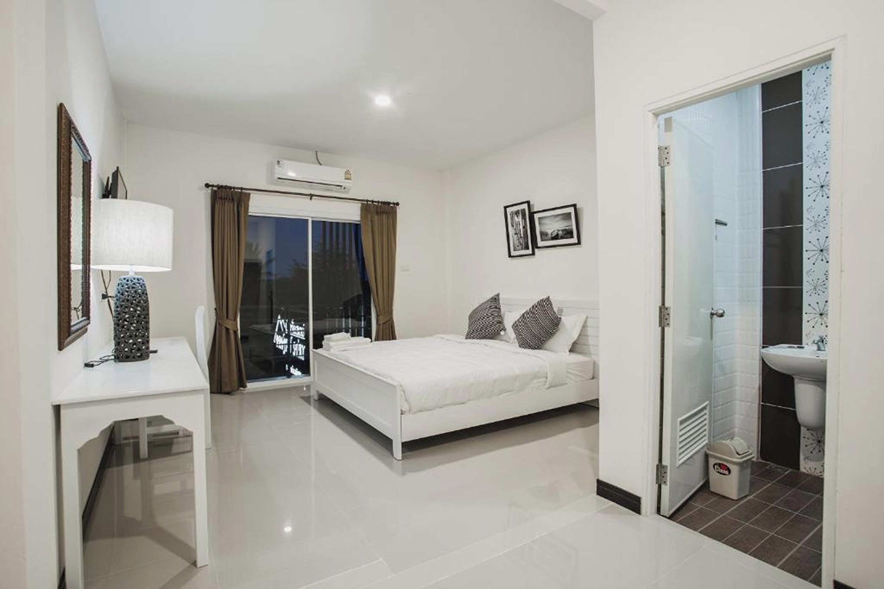 A modern hotel room with a bed, a desk, a bathroom, and a sliding glass door to a balcony.