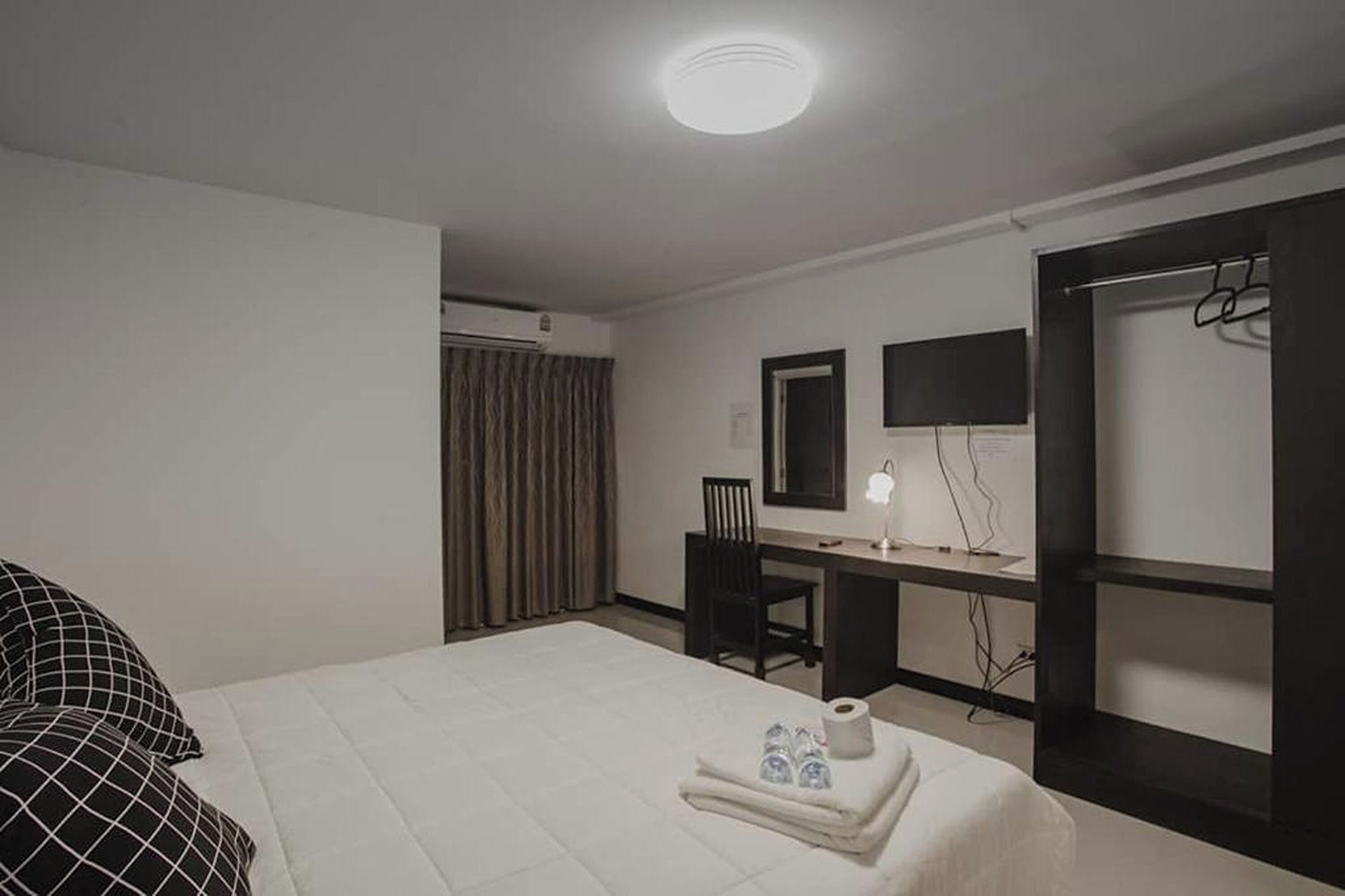 A hotel room with a bed, a desk with a chair, a mirror, a wardrobe, and a shower area.