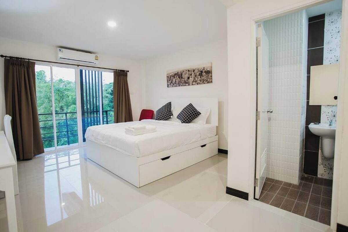 Un dormitorio moderno con una cama grande, una silla roja, una mesita de noche blanca y un baño con lavamanos y espejo.