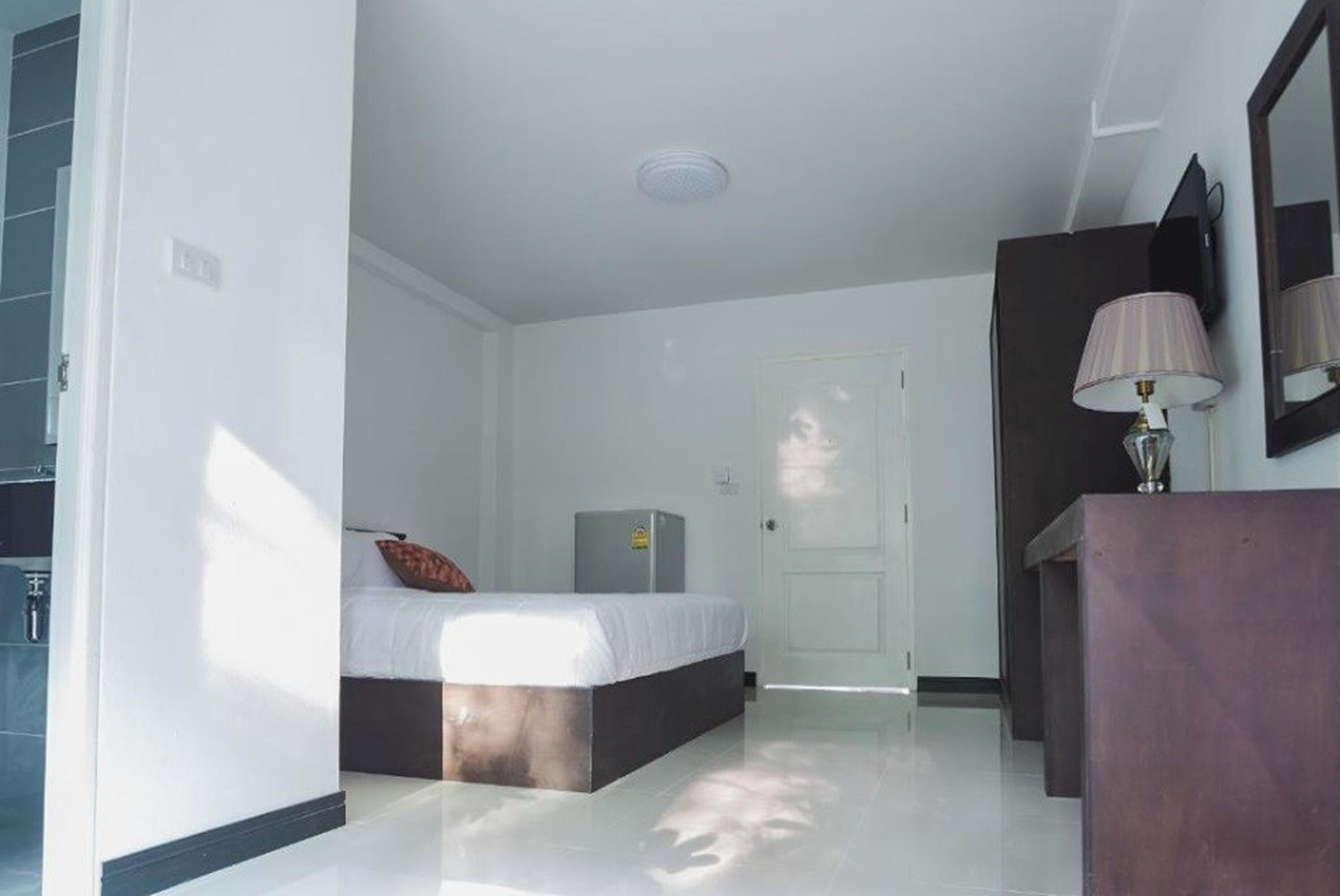A hotel room with a bed, a desk, a lamp, and a door.