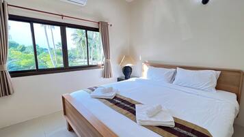 A hotel room with a large bed, a nightstand with a lamp, a window with curtains, and an air conditioning unit.
