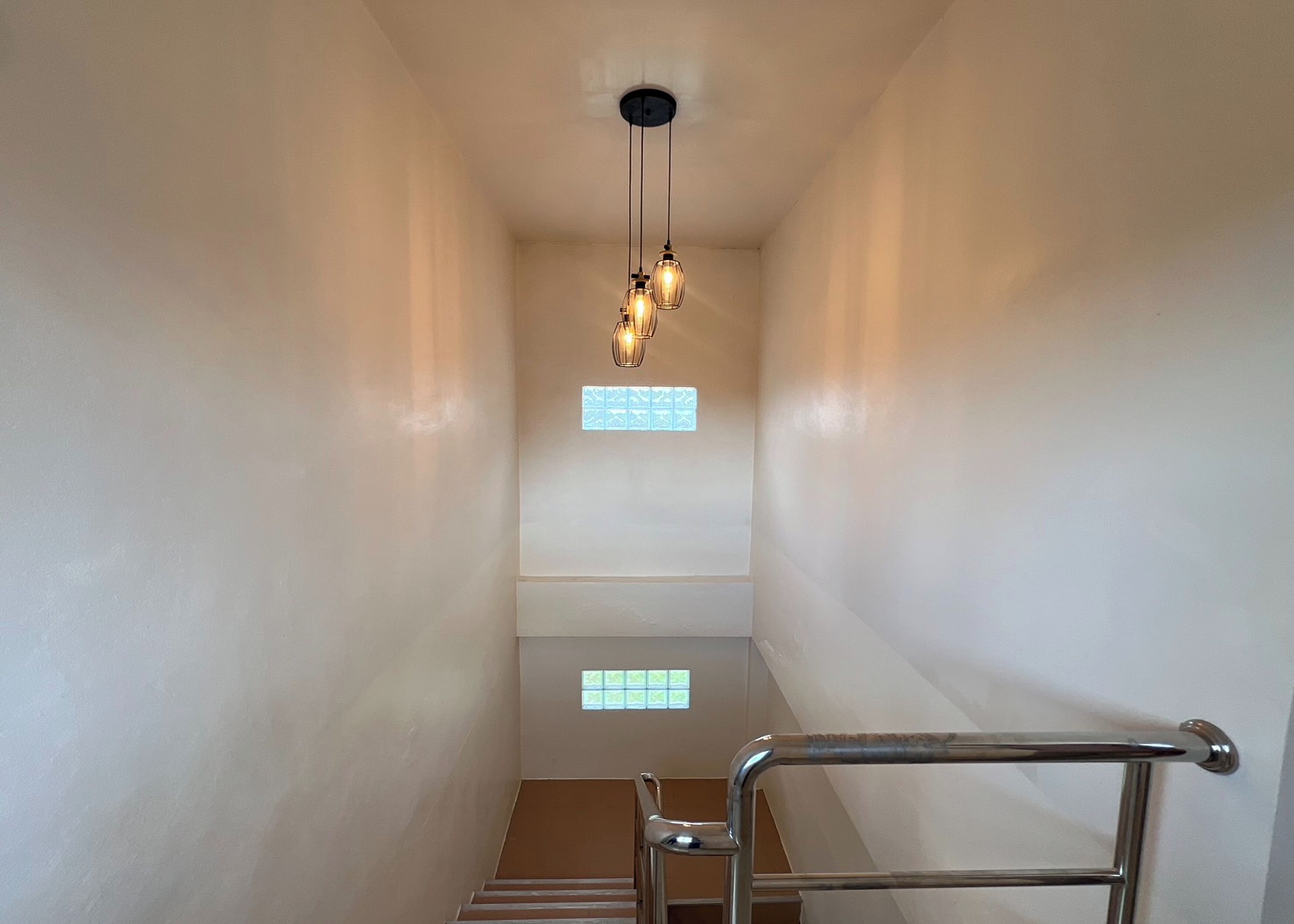 Una stretta scala con ringhiera in metallo, un lampadario e due piccole finestre con vetro decorato.