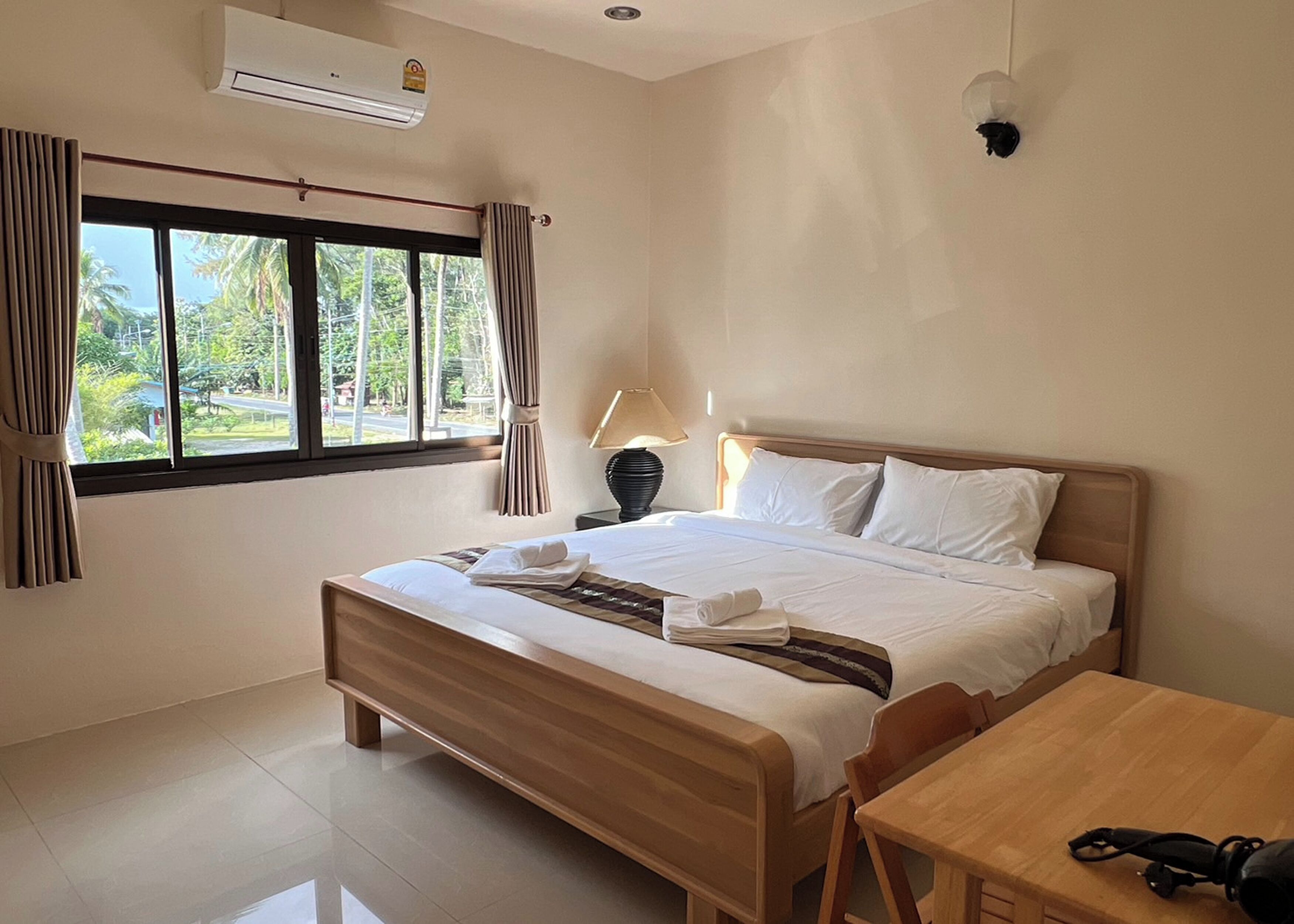 A hotel room with a bed, a table, a lamp, and a window with curtains.