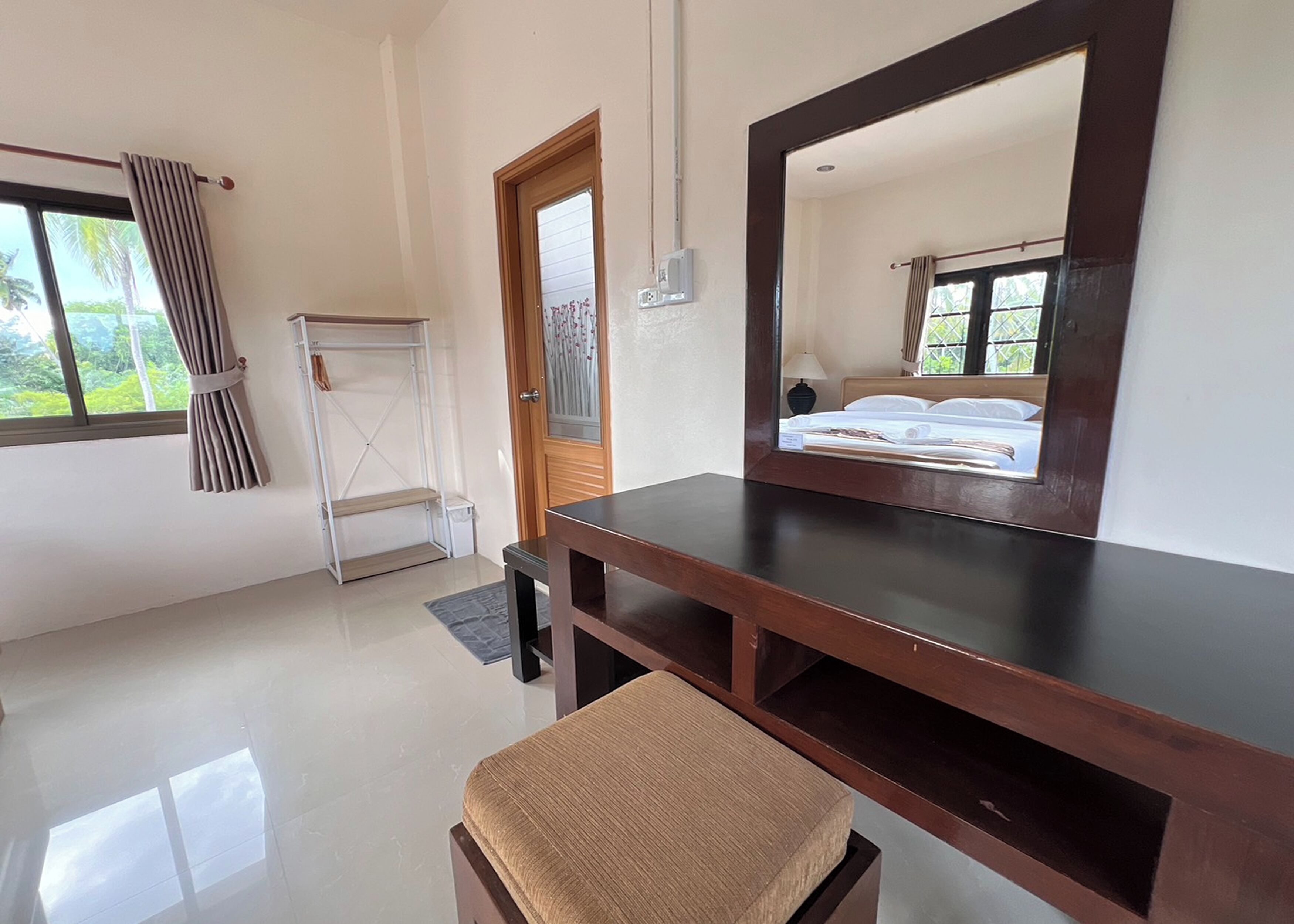 A room with a wooden desk, a chair, a bed with a headboard, a window with curtains, and a door.