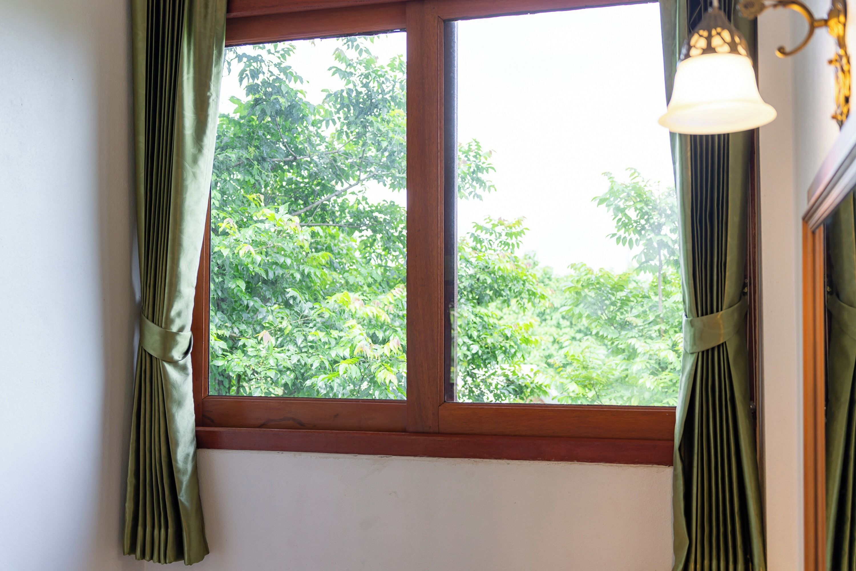 A window with green curtains, a wooden frame, and a hanging light fixture.