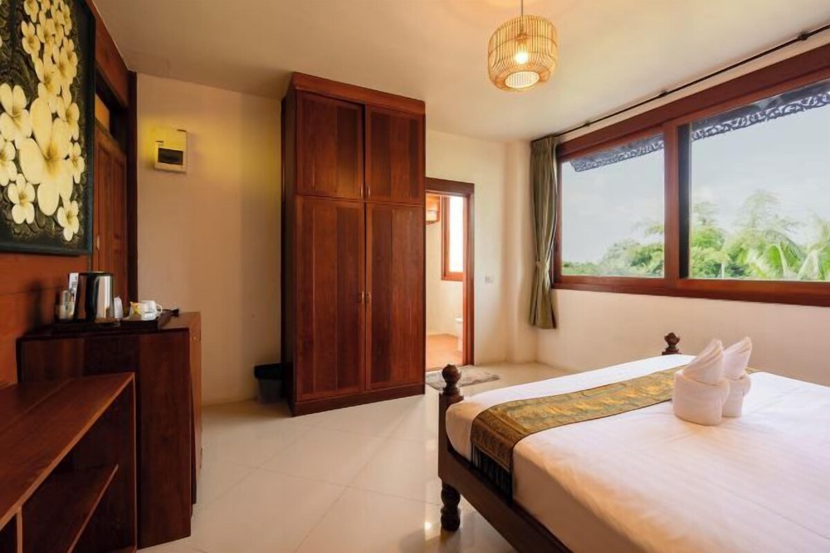 Un dormitorio con cama, armario de madera y vista a la vegetación por una ventana.