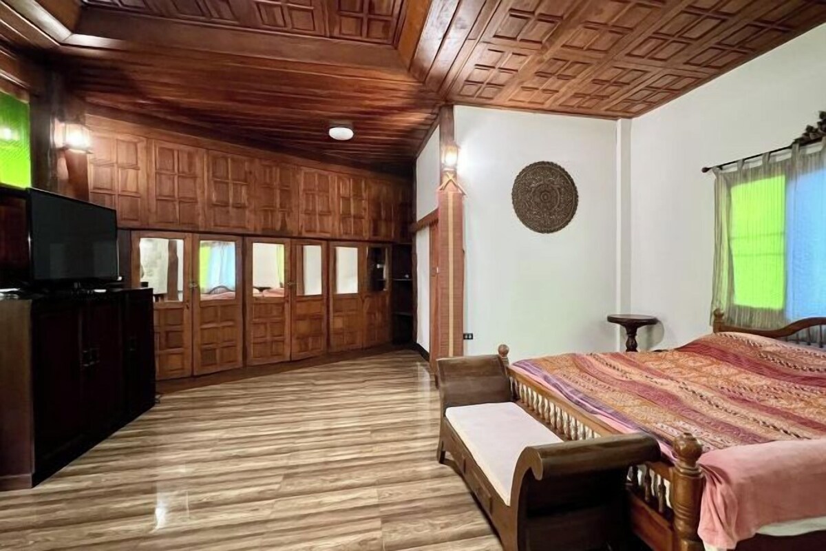 Una habitación con paneles de madera, una cama con colcha estampada, un televisor sobre un mueble bajo y un adorno circular en la pared.