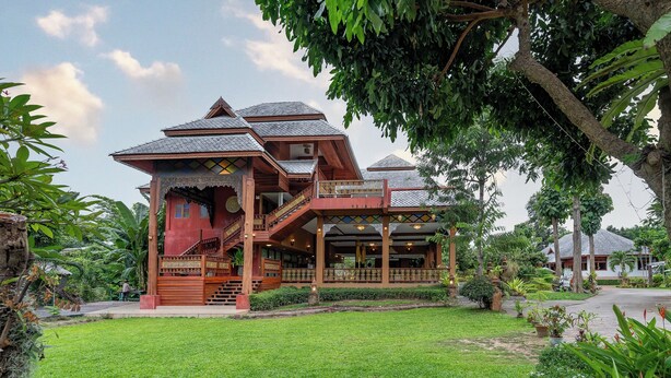 Une maison traditionnelle en bois, dotée d’un balcon, entourée d’une végétation luxuriante et d’une pelouse bien entretenue.
