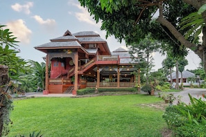 A traditional wooden house with a balcony, surrounded by lush greenery and a well-maintained lawn. - Romsak Lanna Resort (Hang Dong)
