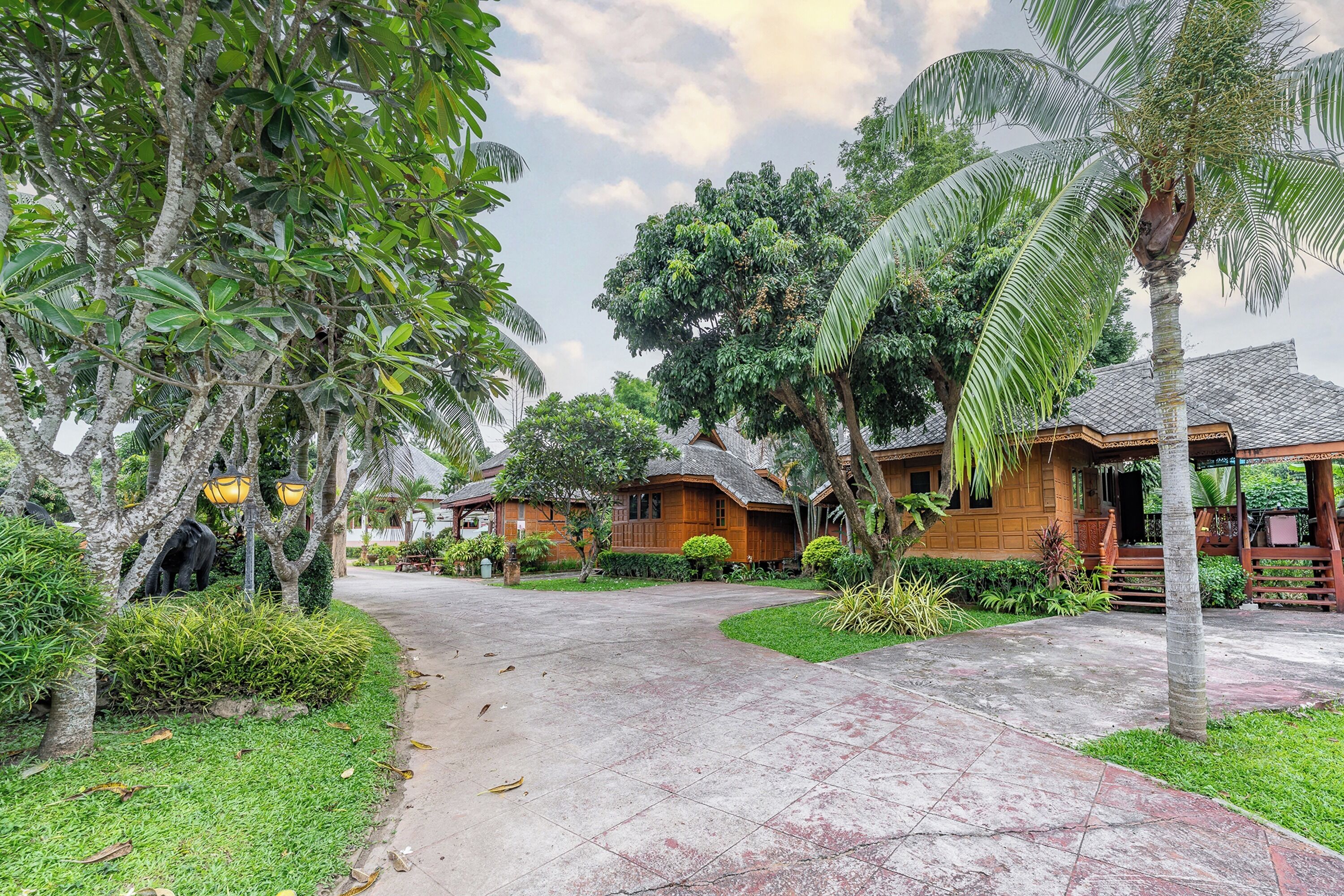 A tropical resort with a paved walkway, wooden buildings, and lush greenery.