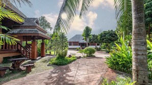 Un bâtiment traditionnel en bois, doté d’un patio carrelé et d’une végétation luxuriante.