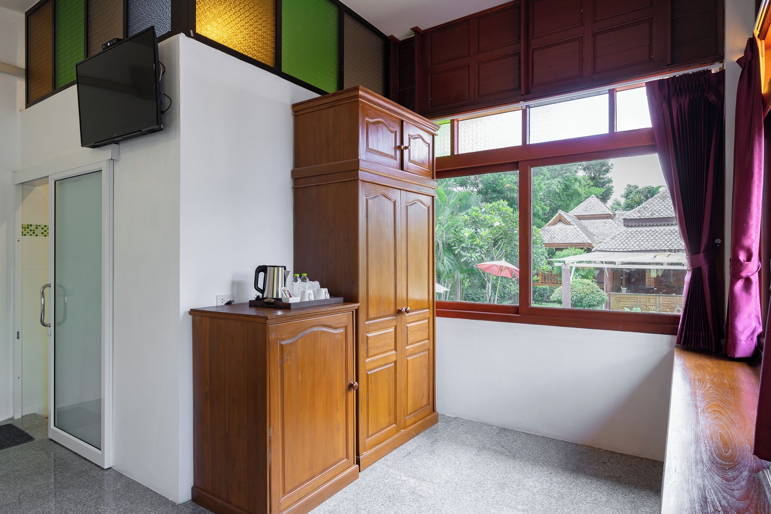 A room with a wooden wardrobe, a television mounted on the wall, and a window with curtains.