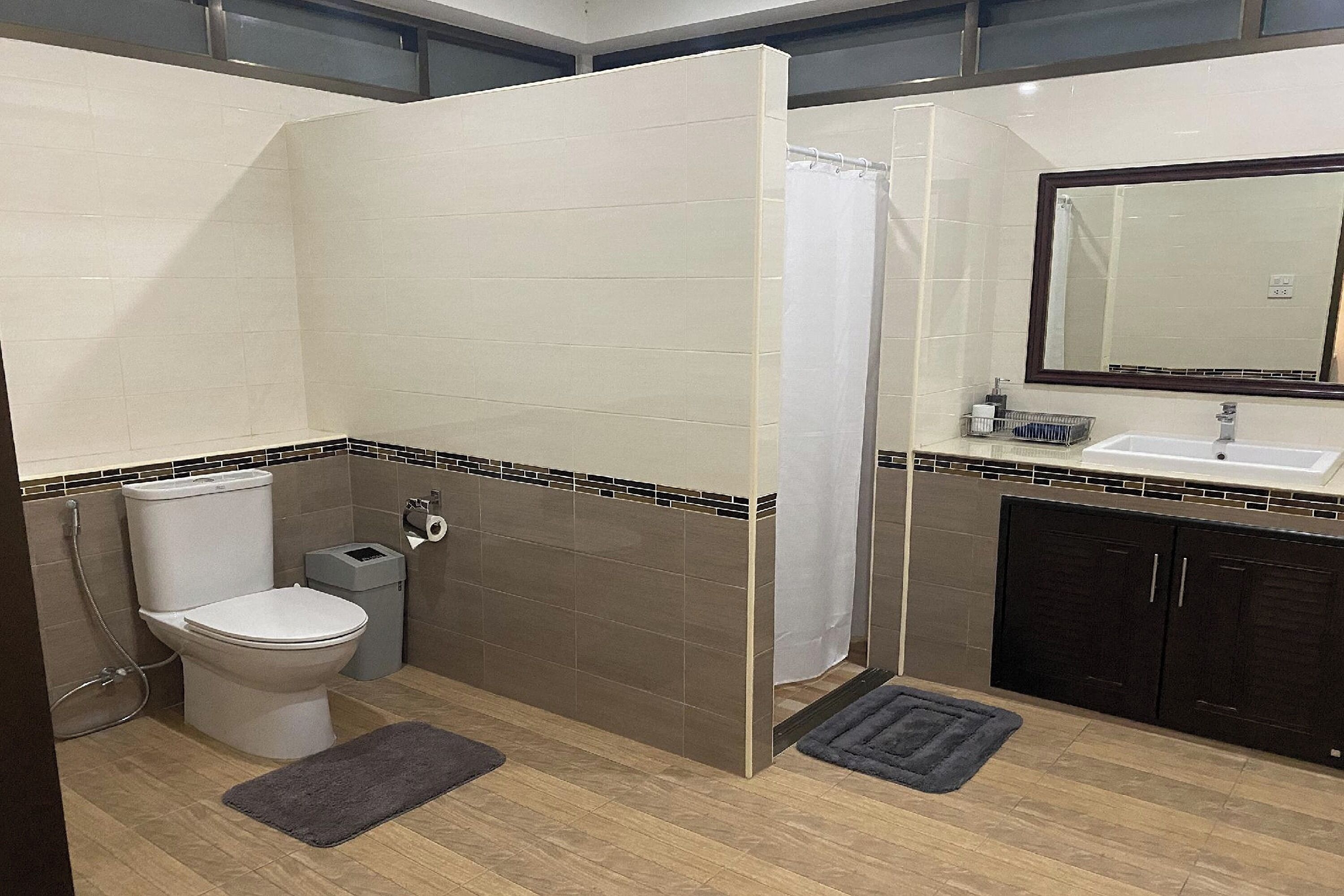 A bathroom with a toilet, shower, sink, and dark cabinets.