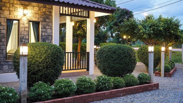A stone building with a covered porch, neatly trimmed hedges, and gravel pathways.
