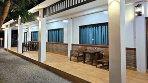 A hotel exterior with a covered outdoor seating area, large windows, and a brick wall.